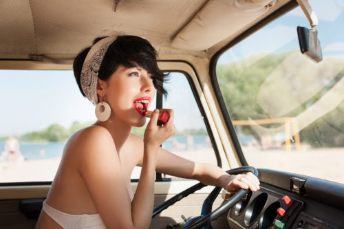 Sensual woman looking in rear view mirror and putting make up in car