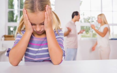 Little girl looking depressed in front of fighting parents in the kitchen